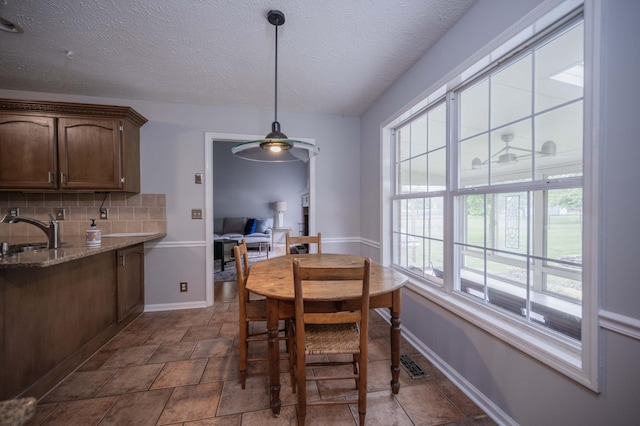 dining room with stone finish floor, ceiling fan, a textured ceiling, visible vents, and baseboards
