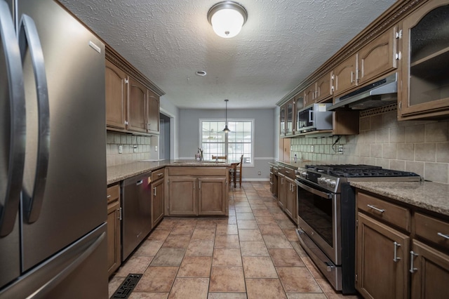 kitchen featuring a peninsula, glass insert cabinets, baseboards, under cabinet range hood, and appliances with stainless steel finishes