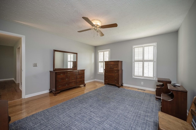 bedroom with a textured ceiling, a ceiling fan, baseboards, wood finished floors, and visible vents