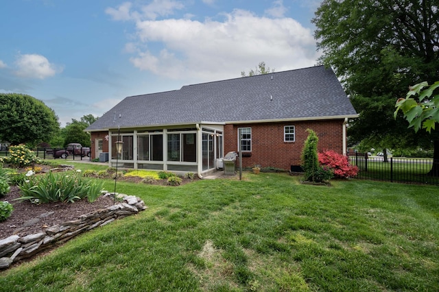 rear view of property featuring fence, a lawn, a sunroom, and roof with shingles