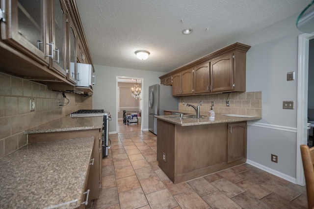 kitchen featuring decorative backsplash, a sink, a peninsula, a chandelier, and stainless steel appliances