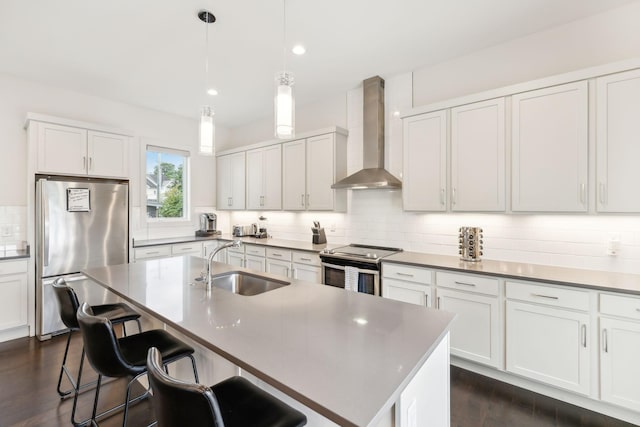 kitchen featuring wall chimney range hood, appliances with stainless steel finishes, a sink, a breakfast bar area, and tasteful backsplash
