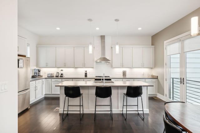 kitchen with freestanding refrigerator, a breakfast bar, wall chimney range hood, a sink, and dark wood finished floors