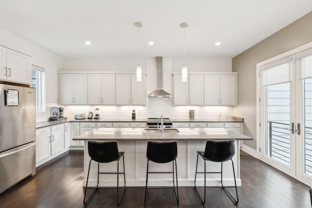 kitchen featuring wall chimney range hood, a kitchen breakfast bar, freestanding refrigerator, and dark wood-style floors