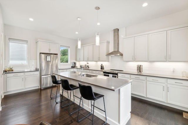 kitchen featuring wall chimney range hood, a breakfast bar area, tasteful backsplash, a sink, and stainless steel appliances