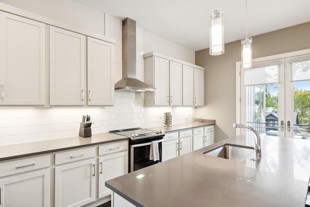 kitchen with wall chimney range hood, white cabinets, stainless steel electric stove, a sink, and decorative light fixtures