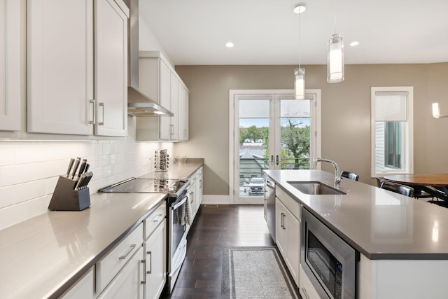 kitchen with a sink, an island with sink, stainless steel appliances, decorative backsplash, and dark wood-style floors