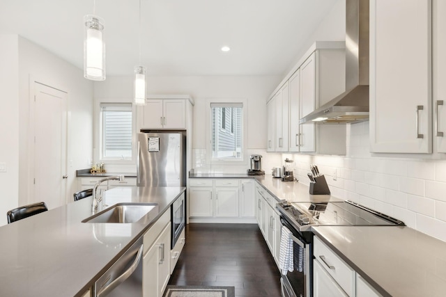 kitchen featuring appliances with stainless steel finishes, a sink, wall chimney exhaust hood, decorative light fixtures, and backsplash