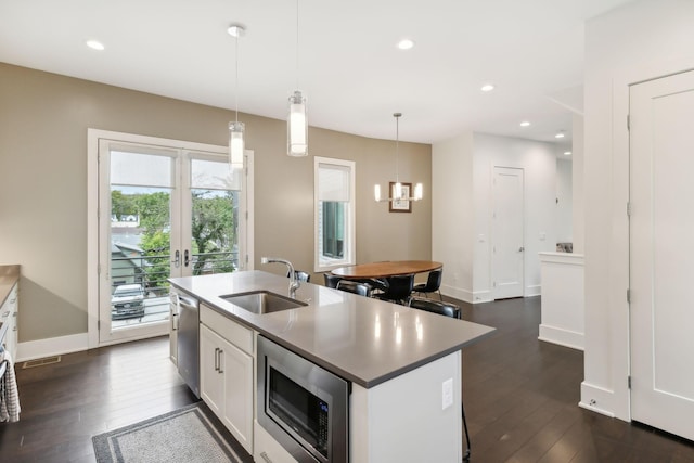 kitchen with dark wood-style flooring, pendant lighting, appliances with stainless steel finishes, a sink, and an island with sink