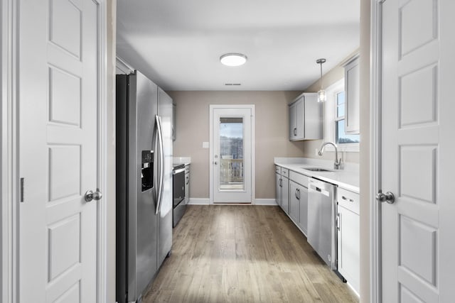 kitchen featuring appliances with stainless steel finishes, a sink, gray cabinetry, light countertops, and light wood finished floors