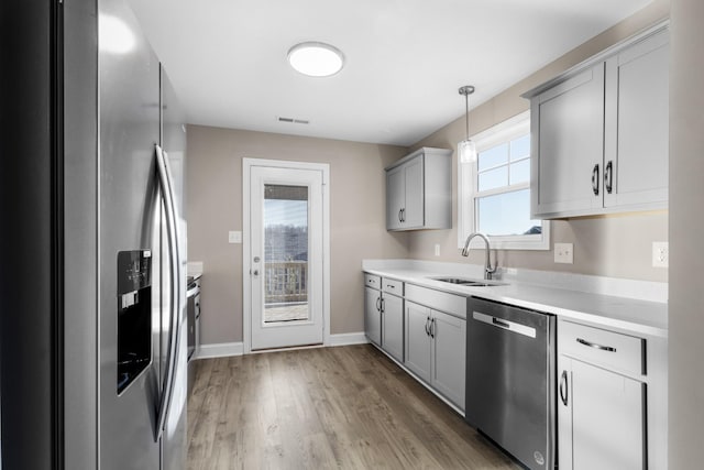 kitchen with appliances with stainless steel finishes, a sink, light countertops, light wood-style flooring, and visible vents