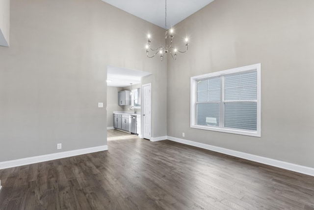 unfurnished dining area featuring dark wood-style flooring, a sink, baseboards, a chandelier, and a high ceiling