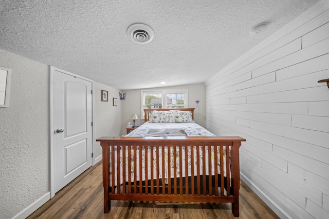 bedroom with baseboards, a textured ceiling, visible vents, and wood finished floors