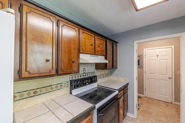 kitchen featuring decorative backsplash, light tile patterned flooring, tile counters, electric range oven, and under cabinet range hood