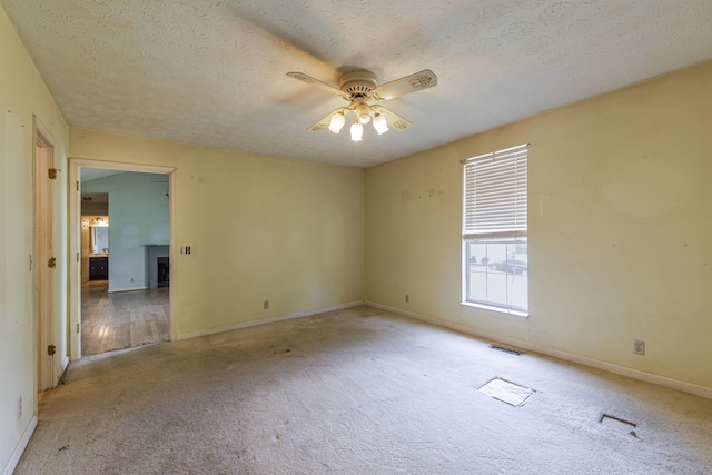 unfurnished room featuring ceiling fan, a textured ceiling, a fireplace, baseboards, and carpet flooring