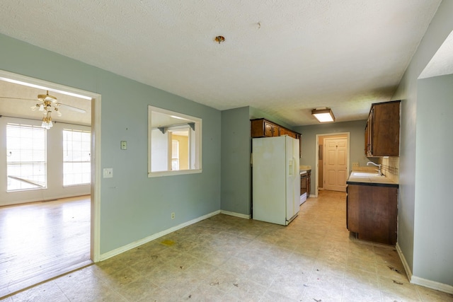 kitchen featuring a sink, baseboards, white fridge with ice dispenser, and light countertops
