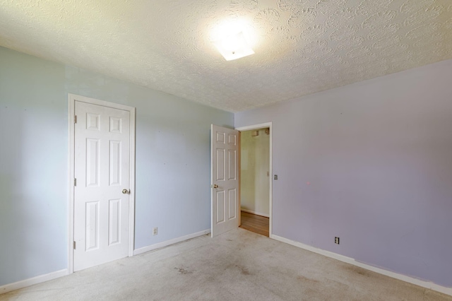 unfurnished bedroom with a textured ceiling, light colored carpet, and baseboards