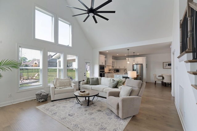 living area with baseboards, a ceiling fan, high vaulted ceiling, and wood finished floors