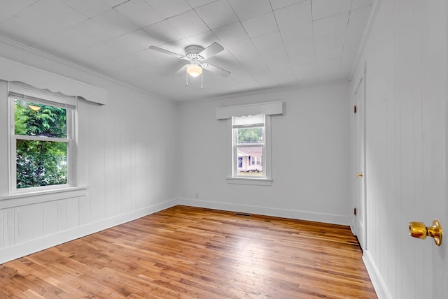 empty room featuring a ceiling fan, baseboards, ornamental molding, and light wood-style floors