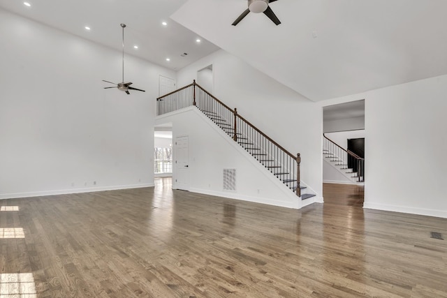 unfurnished living room featuring stairs, a ceiling fan, baseboards, and wood finished floors
