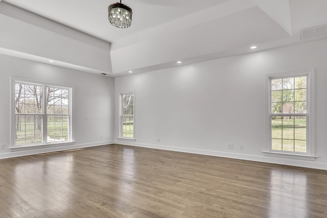 empty room with plenty of natural light, wood finished floors, a notable chandelier, and visible vents