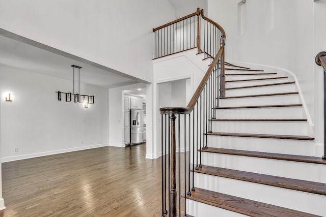 stairs with baseboards, wood finished floors, and a high ceiling