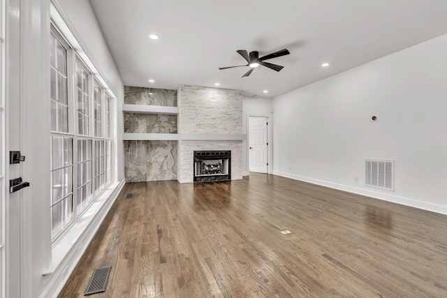 unfurnished living room with visible vents, ceiling fan, wood finished floors, and a stone fireplace