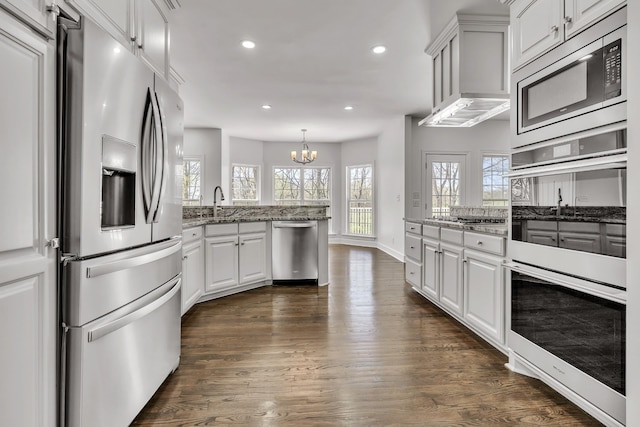 kitchen with appliances with stainless steel finishes, light stone countertops, a peninsula, an inviting chandelier, and recessed lighting