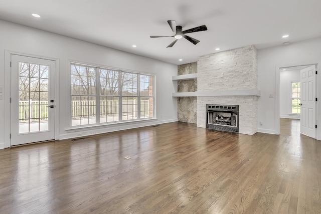 unfurnished living room with a ceiling fan, a stone fireplace, visible vents, wood finished floors, and recessed lighting