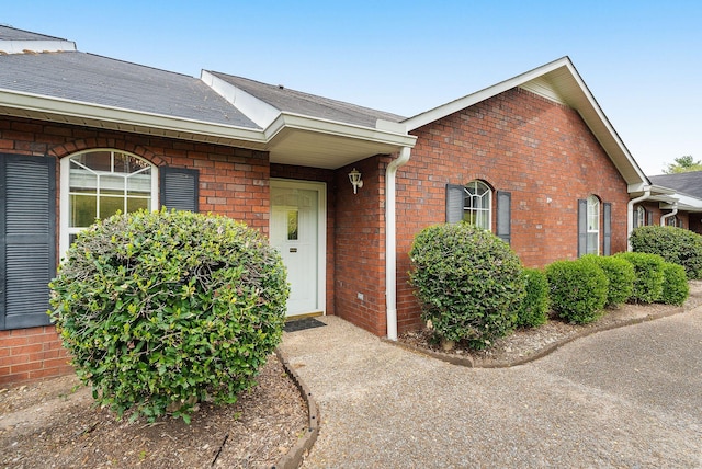 view of exterior entry with brick siding and roof with shingles
