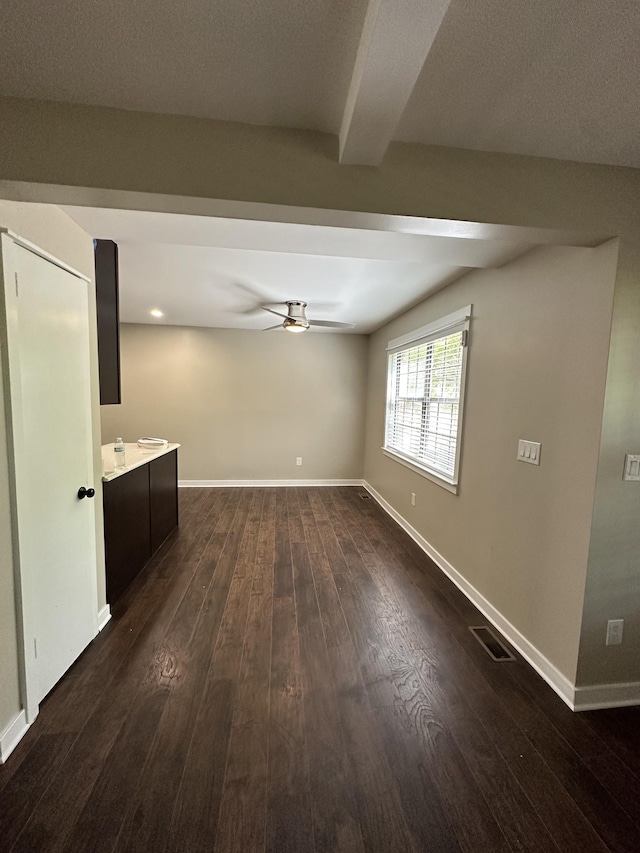 spare room featuring baseboards, ceiling fan, dark wood-type flooring, and visible vents