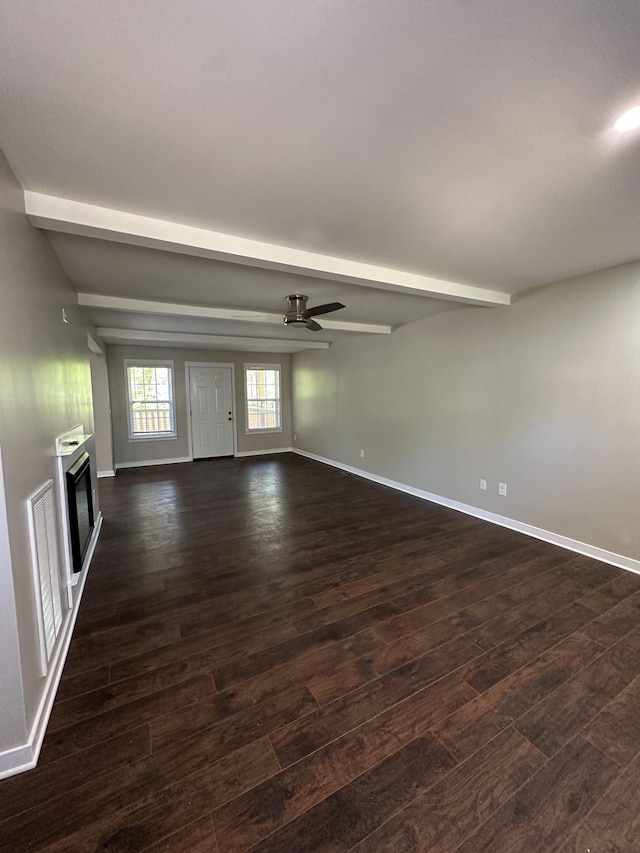 empty room featuring a glass covered fireplace, beamed ceiling, baseboards, dark wood-style floors, and a ceiling fan