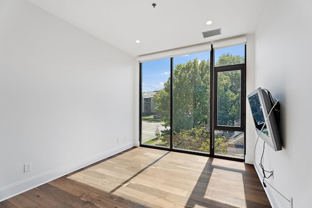 spare room featuring expansive windows, baseboards, wood finished floors, and visible vents