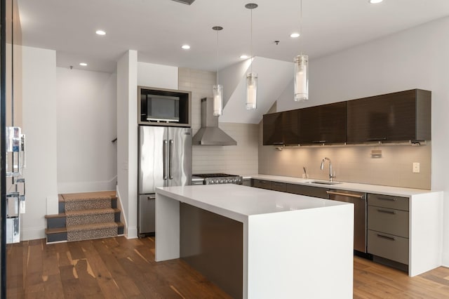 kitchen featuring a kitchen island, appliances with stainless steel finishes, a sink, light countertops, and wall chimney exhaust hood