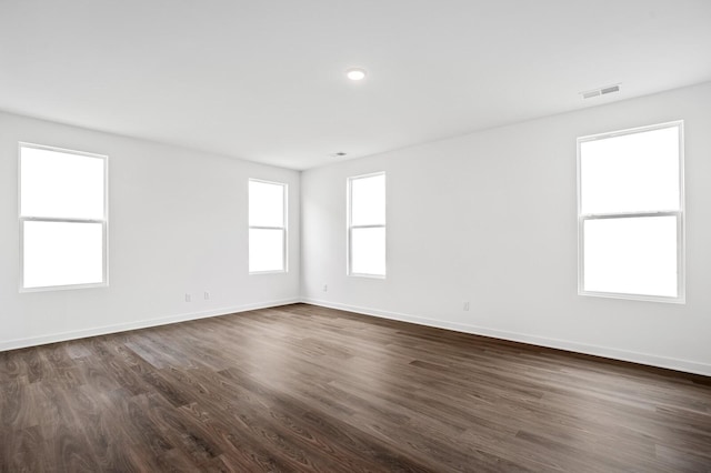 empty room featuring visible vents, dark wood finished floors, and baseboards