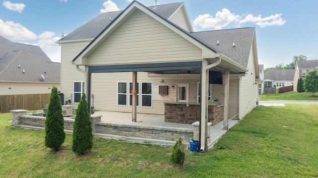 rear view of property featuring a patio, a shingled roof, a lawn, and fence