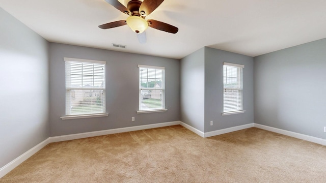 empty room featuring a wealth of natural light, light colored carpet, and visible vents