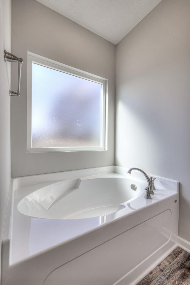 bathroom featuring a garden tub, baseboards, and wood finished floors