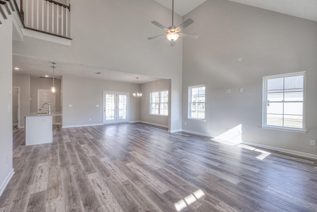 unfurnished living room featuring ceiling fan with notable chandelier, wood finished floors, and high vaulted ceiling