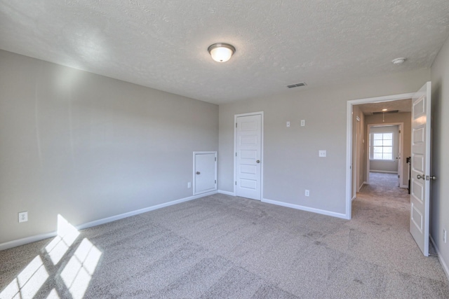 unfurnished bedroom with attic access, a textured ceiling, visible vents, light colored carpet, and baseboards