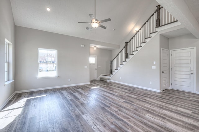 unfurnished living room with high vaulted ceiling, stairs, a ceiling fan, baseboards, and wood finished floors