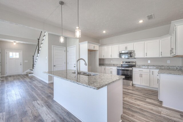 kitchen with appliances with stainless steel finishes, a sink, a textured ceiling, an island with sink, and visible vents