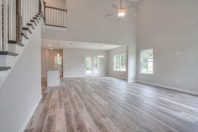 unfurnished living room featuring baseboards, ceiling fan with notable chandelier, light wood finished floors, and a towering ceiling