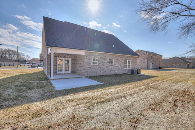 rear view of property featuring french doors, a lawn, central AC unit, brick siding, and a shingled roof