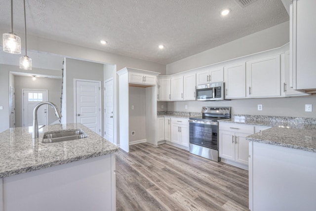 kitchen featuring a textured ceiling, light wood-type flooring, a sink, white cabinets, and stainless steel appliances