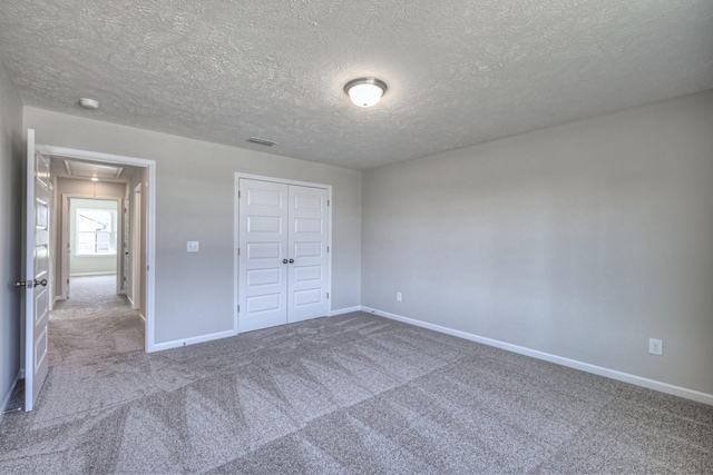 unfurnished bedroom with attic access, a textured ceiling, baseboards, a closet, and carpet flooring