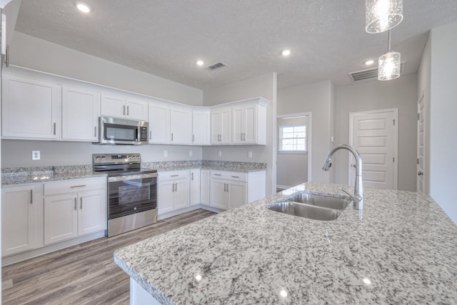 kitchen featuring light wood-type flooring, a textured ceiling, white cabinets, a sink, and appliances with stainless steel finishes