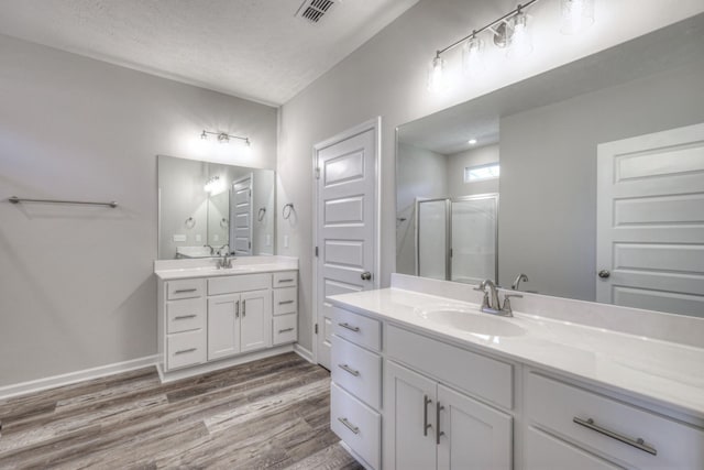 bathroom with visible vents, wood finished floors, two vanities, a sink, and a stall shower