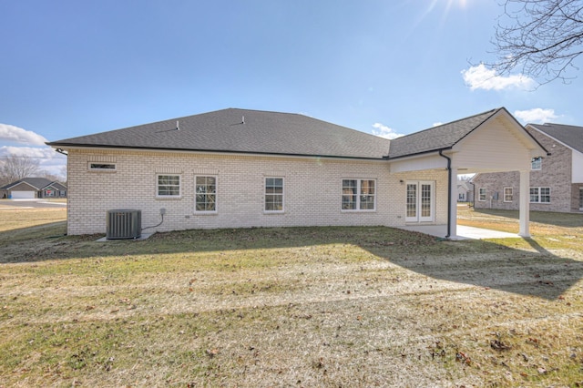 back of property featuring cooling unit, roof with shingles, brick siding, a patio area, and a lawn