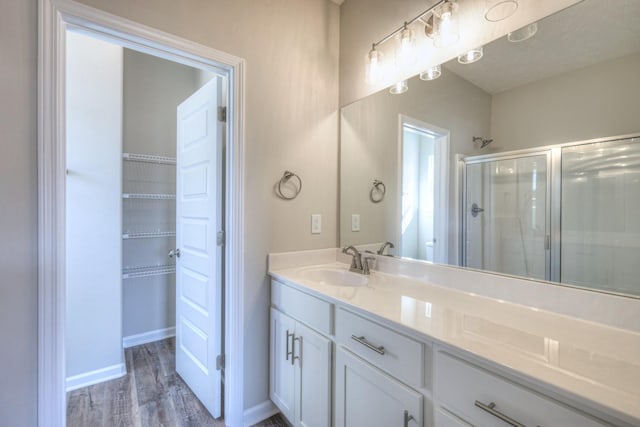 bathroom with wood finished floors, baseboards, a stall shower, and vanity